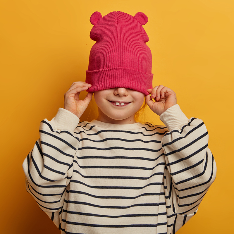 Hüte probieren. Offenes Programm in der Ausstellung Mädchen lächelt und zieht sich dabei ihre Mütze mit Teddyohren über die Augen