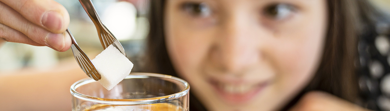 Pressefoto: Mädchen gibt einen Würfel Zucker in ein Glas