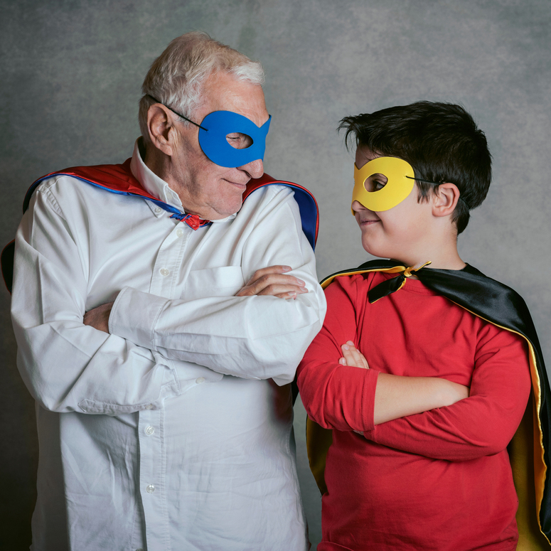 Grossvater mit Enkel als Superheld verkleidet auf grauem Hintergrund