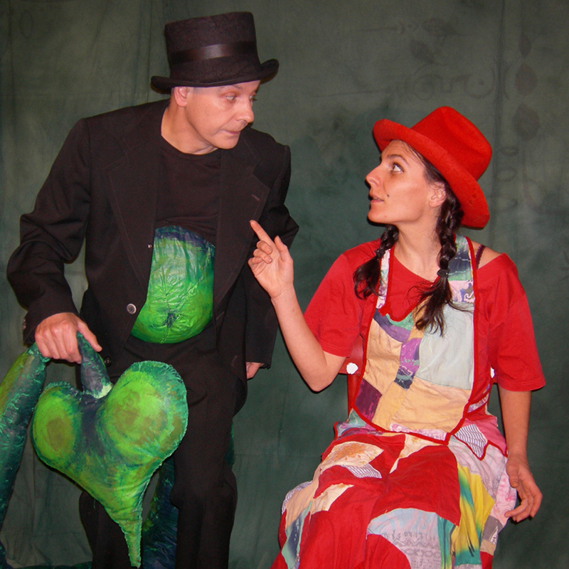 Schauspieler mit Zylinder im Gespräch mit Schauspielerin in rotem Flickenkleid