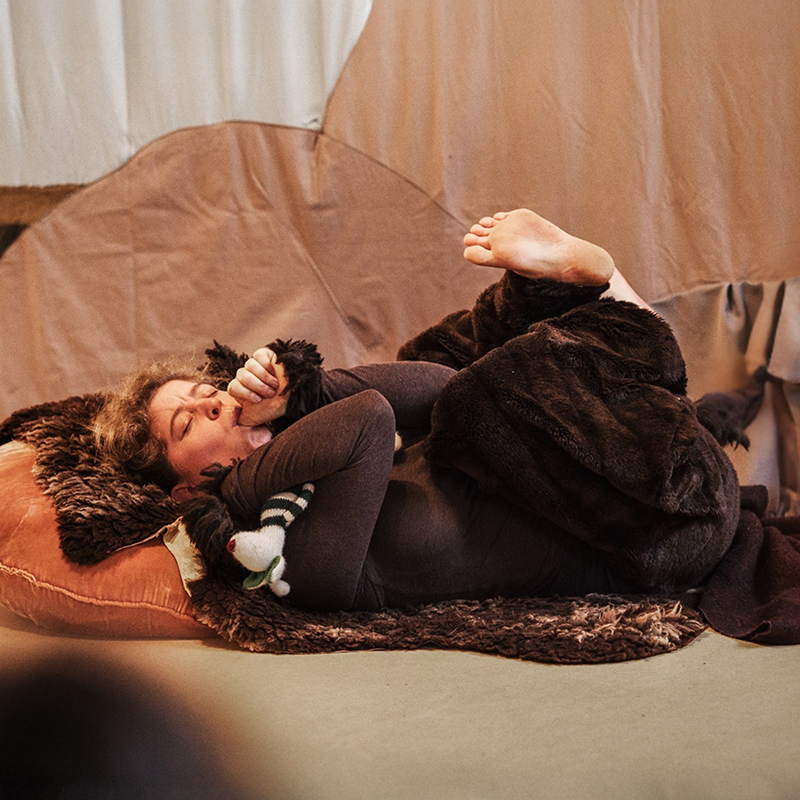 Sujetfoto Theater: Schauspielerin in Bärenkostüm liegt schlafend, Daumen im Mund