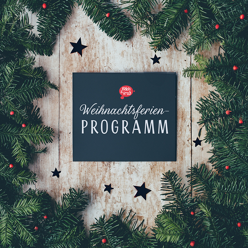 Schwarzes Blattpapier mit "Weihnachtsferien-Programm" beschriftet, umgeben von Tannenzweigen und Sternen.