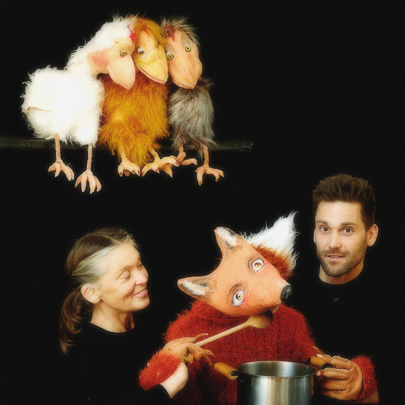 Pressefoto Theater: zwei Personen spielen eine Fuchs-Handpuppe, darüber sitzen 3 Hühner-Handpuppen auf einer Hühnerleiter