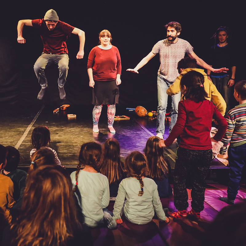 Theaterfoto, Gruppe von Schauspielern steht auf der Bühne. Kinder sitzen im Publikum