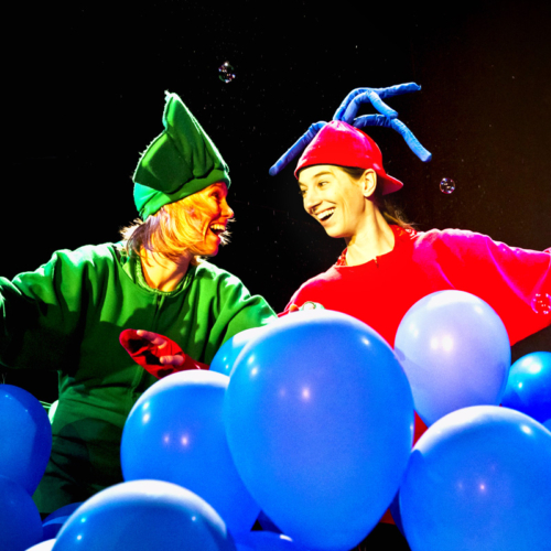 Zwei Schauspielerinnen in Kostümen zwischen blauen Luftballons