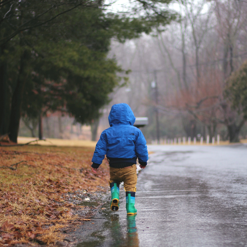 Kind läuft mit Gummistiefeln durch den Regen